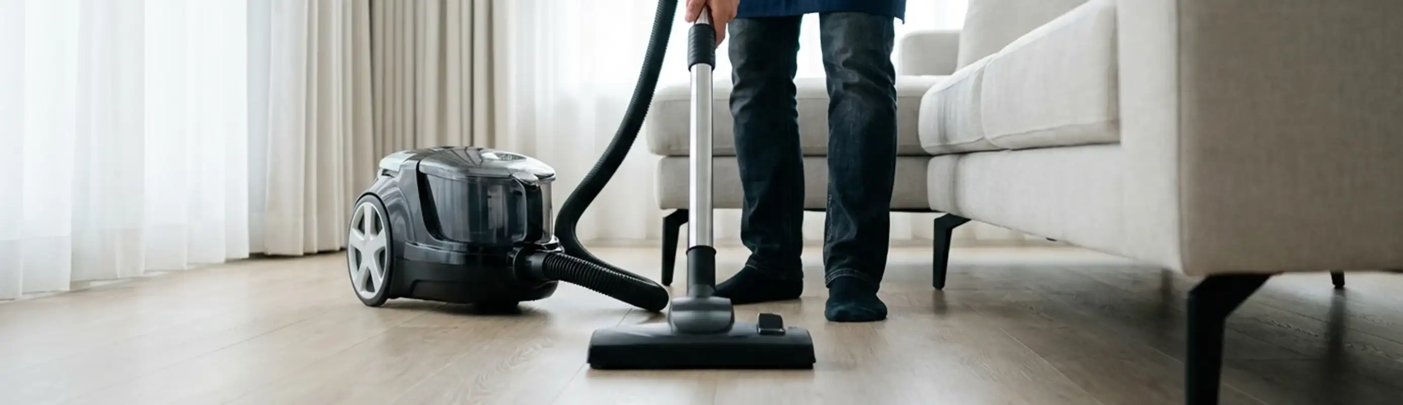 Professional house cleaner vacuuming a living room floor with a canister vacuum cleaner, Riverside, CA.