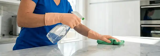 Maid service worker spraying and wiping a kitchen countertop with a microfiber cloth for sanitizing, Riverside, CA.