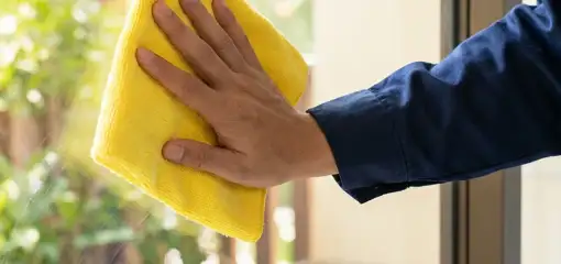 House cleaner wiping a glass window with a yellow microfiber cloth for streak-free cleaning, Riverside, CA.